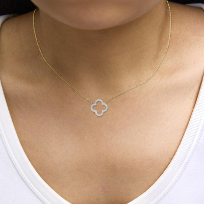 Yellow metal necklace with a quatrefoil pendant encrusted with round white gemstones in prong settings, shown worn on a model, close-up front angle.