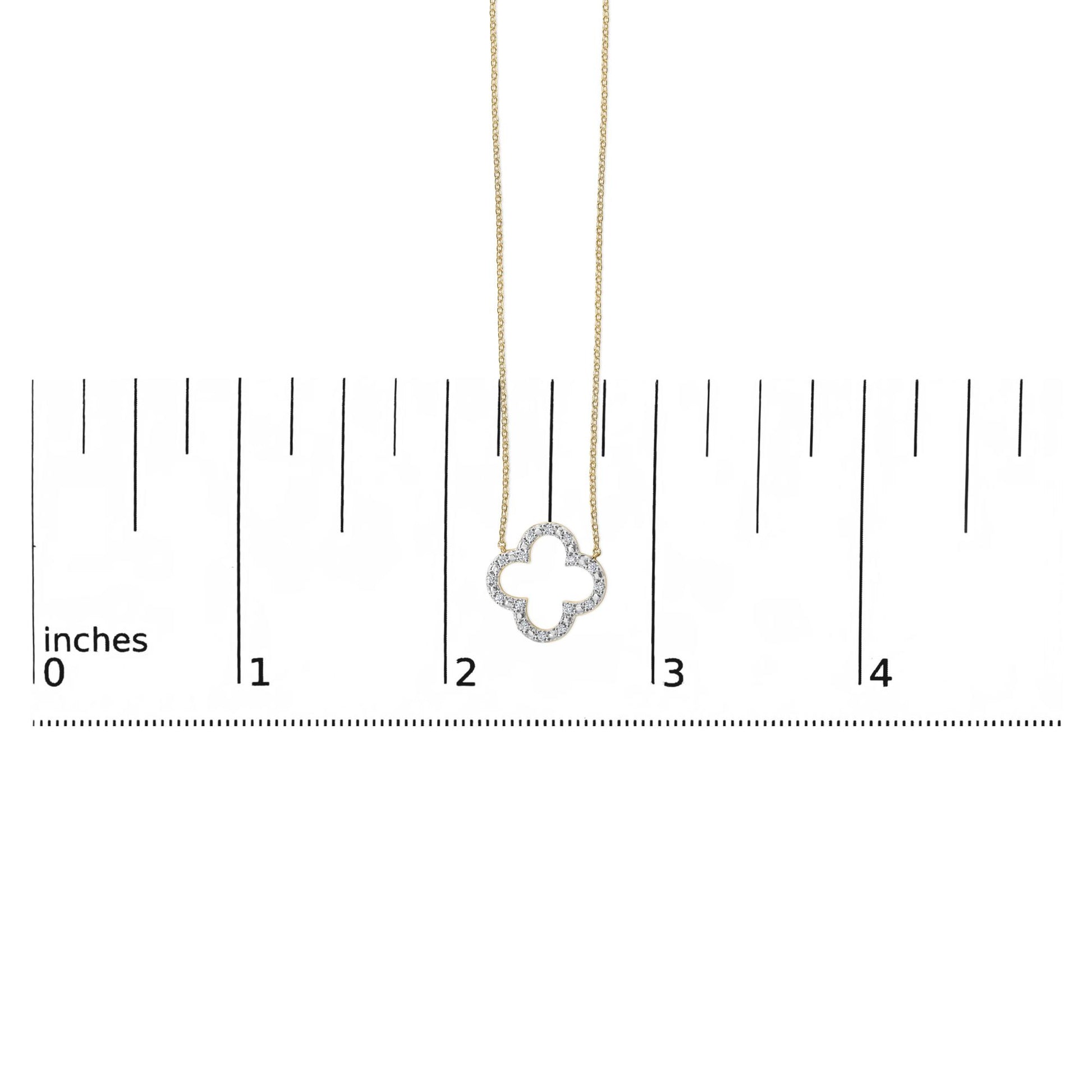 Yellow metal necklace with a clover-shaped pendant featuring round white gemstones in prong setting, shown on a scale from a front angle.
