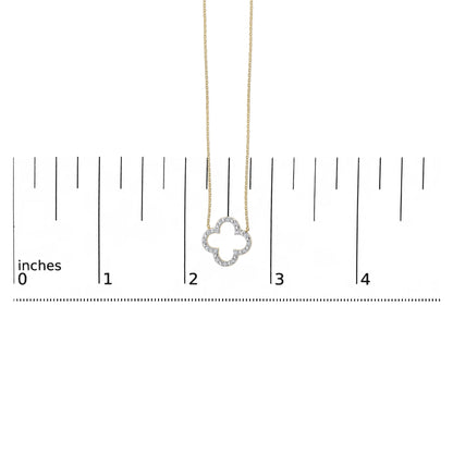 Yellow metal necklace with a clover-shaped pendant featuring round white gemstones in prong setting, shown on a scale from a front angle.