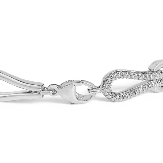 Close-up angled view of a white bracelet with a clasp and a heart-shaped link featuring pave-set round white gemstones.