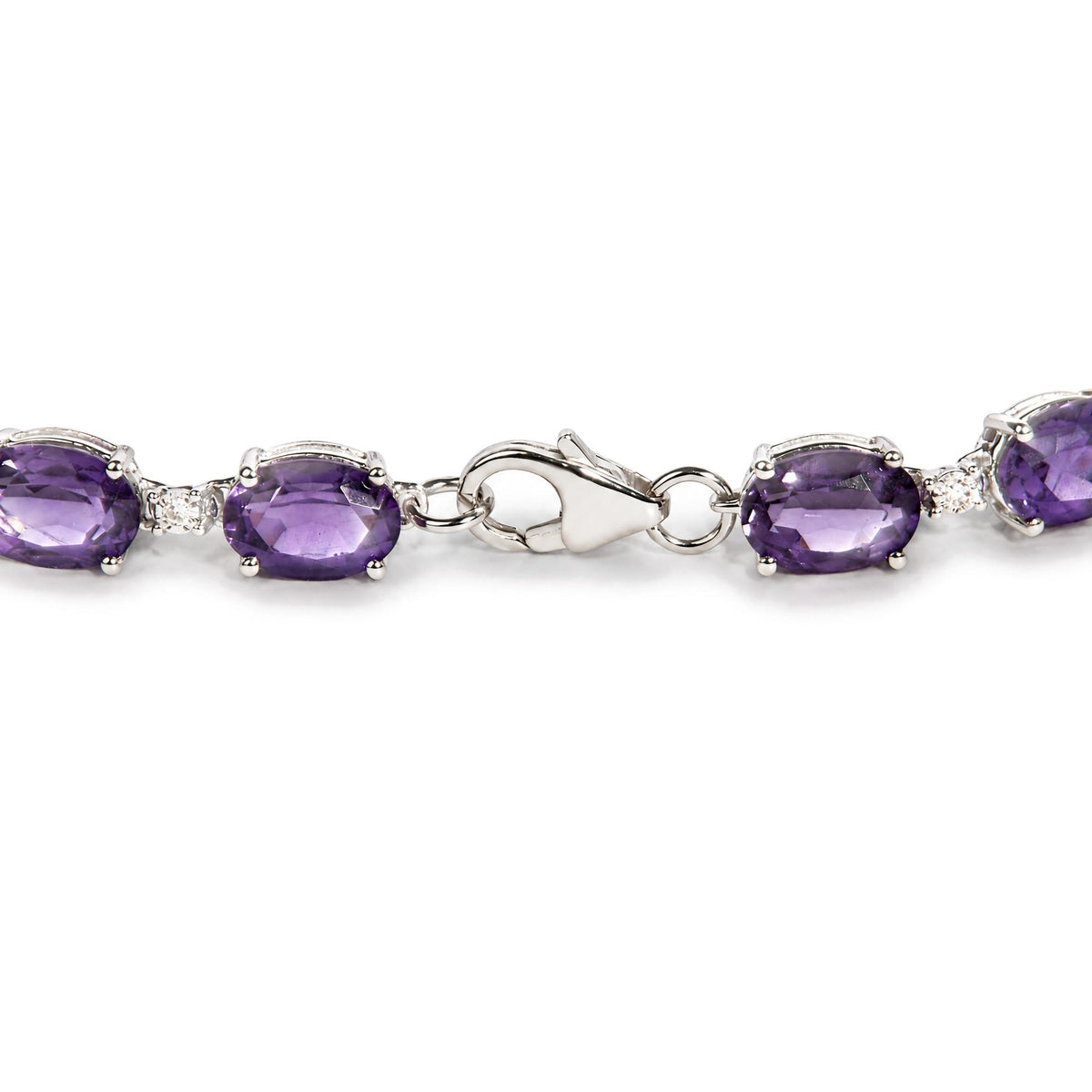 Close-up front angle shot of a white metal bracelet with oval purple gemstones and round white gemstones in prong settings, shown on a scale.