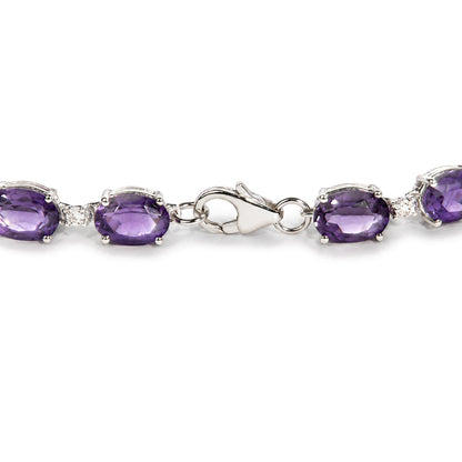 Close-up front angle shot of a white metal bracelet with oval purple gemstones and round white gemstones in prong settings, shown on a scale.