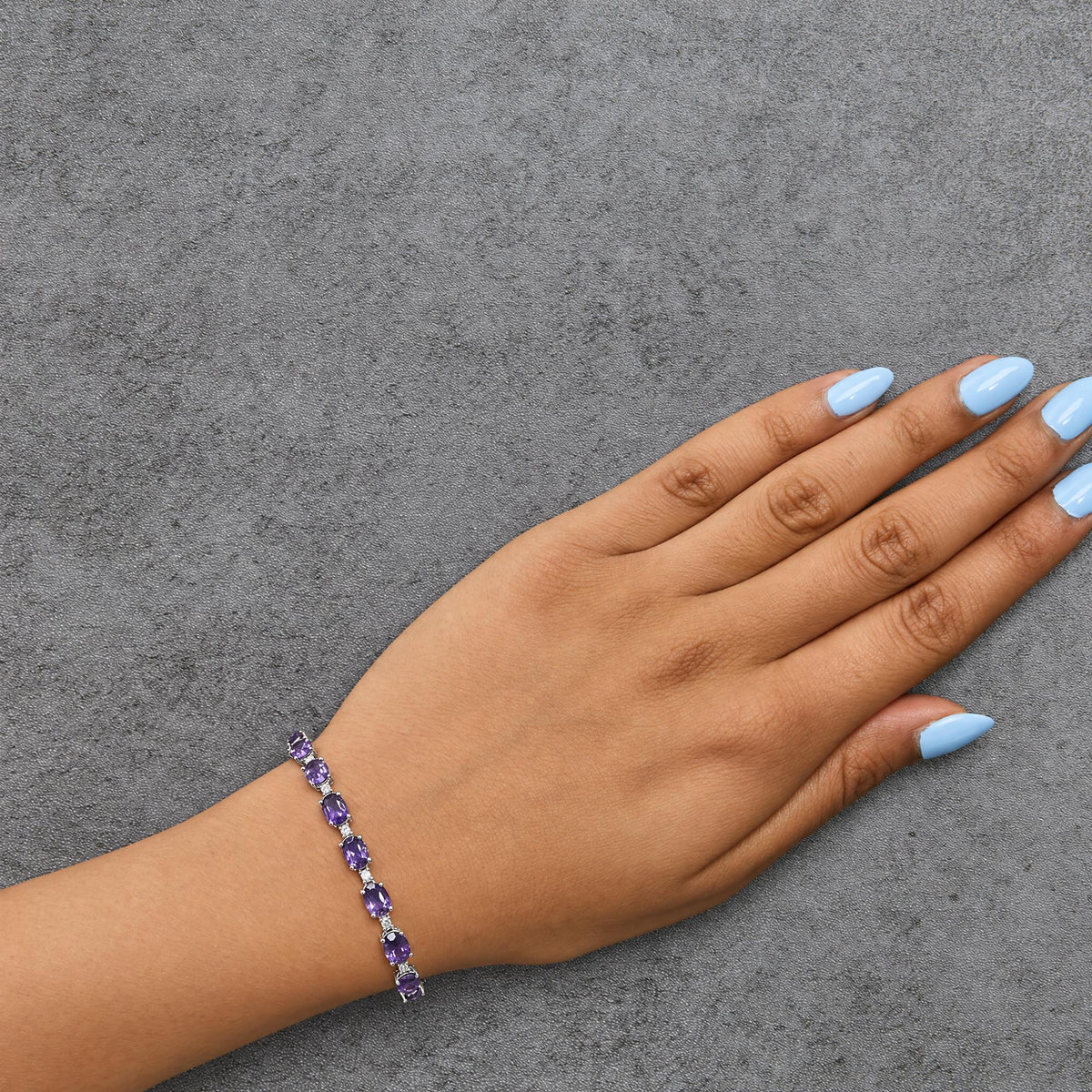 Bracelet with alternating oval purple gemstones and round white gemstones in prong settings, shown worn on a model's wrist, angled top-down.