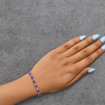 Bracelet with alternating oval purple gemstones and round white gemstones in prong settings, shown worn on a model's wrist, angled top-down.