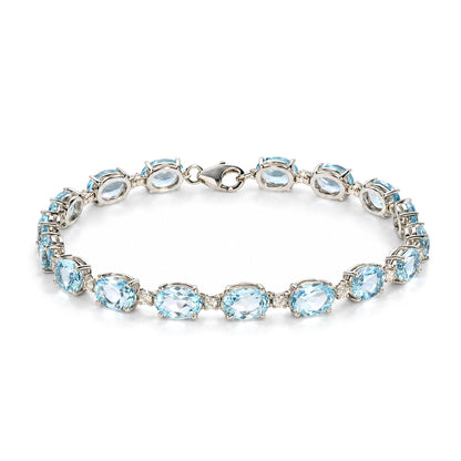 Close-up angled top view of a white metal bracelet featuring oval blue gemstones and small round white gemstones in prong settings, shown on a white background.