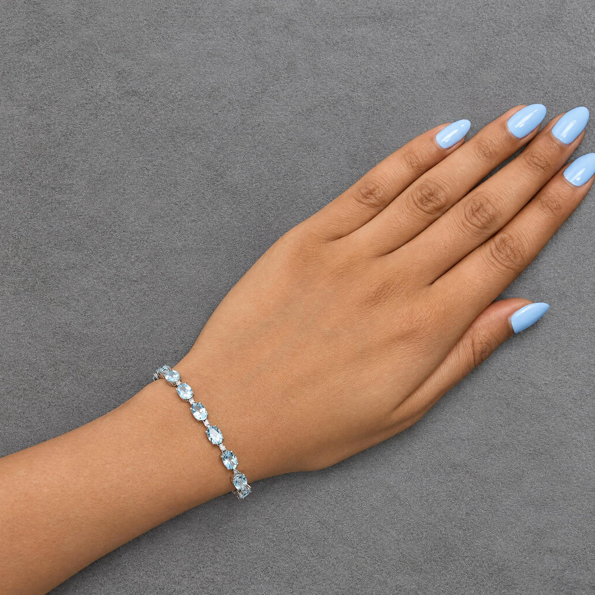 Bracelet with oval blue gemstones and small white round gemstones in prong settings on white metal, shown worn on a model's wrist in a top-down angle.