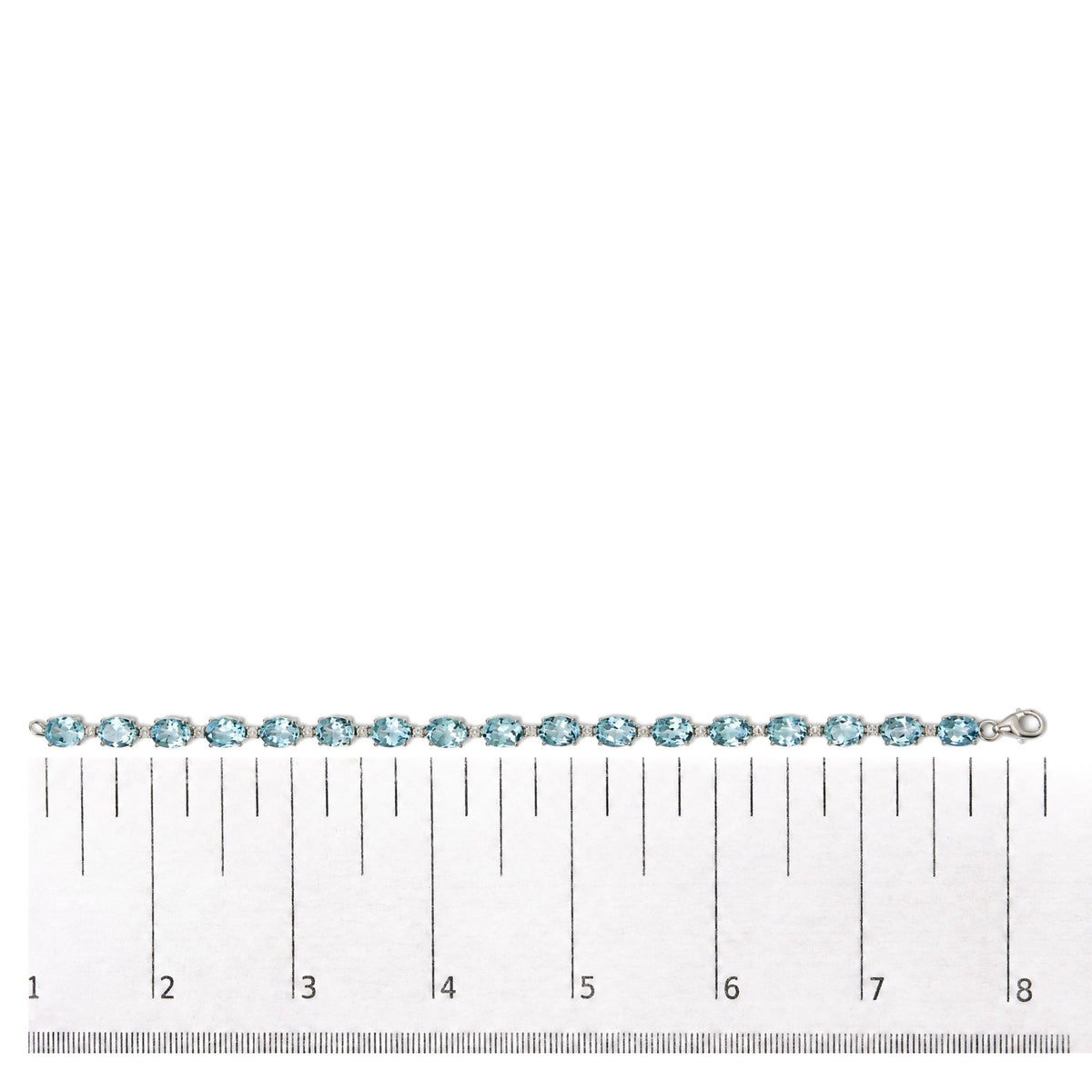 White metal bracelet with alternating blue oval gemstones and small white round gemstones in prong settings, shown flat on a scale, top-down angle.
