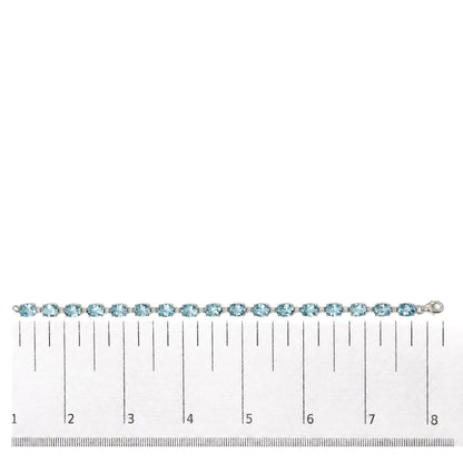 White metal bracelet with alternating blue oval gemstones and small white round gemstones in prong settings, shown flat on a scale, top-down angle.