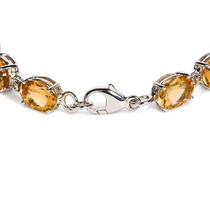 Close-up, angled shot of a white metal bracelet with oval yellow gemstones and small round white gemstones in prong settings, showing the lobster clasp.
