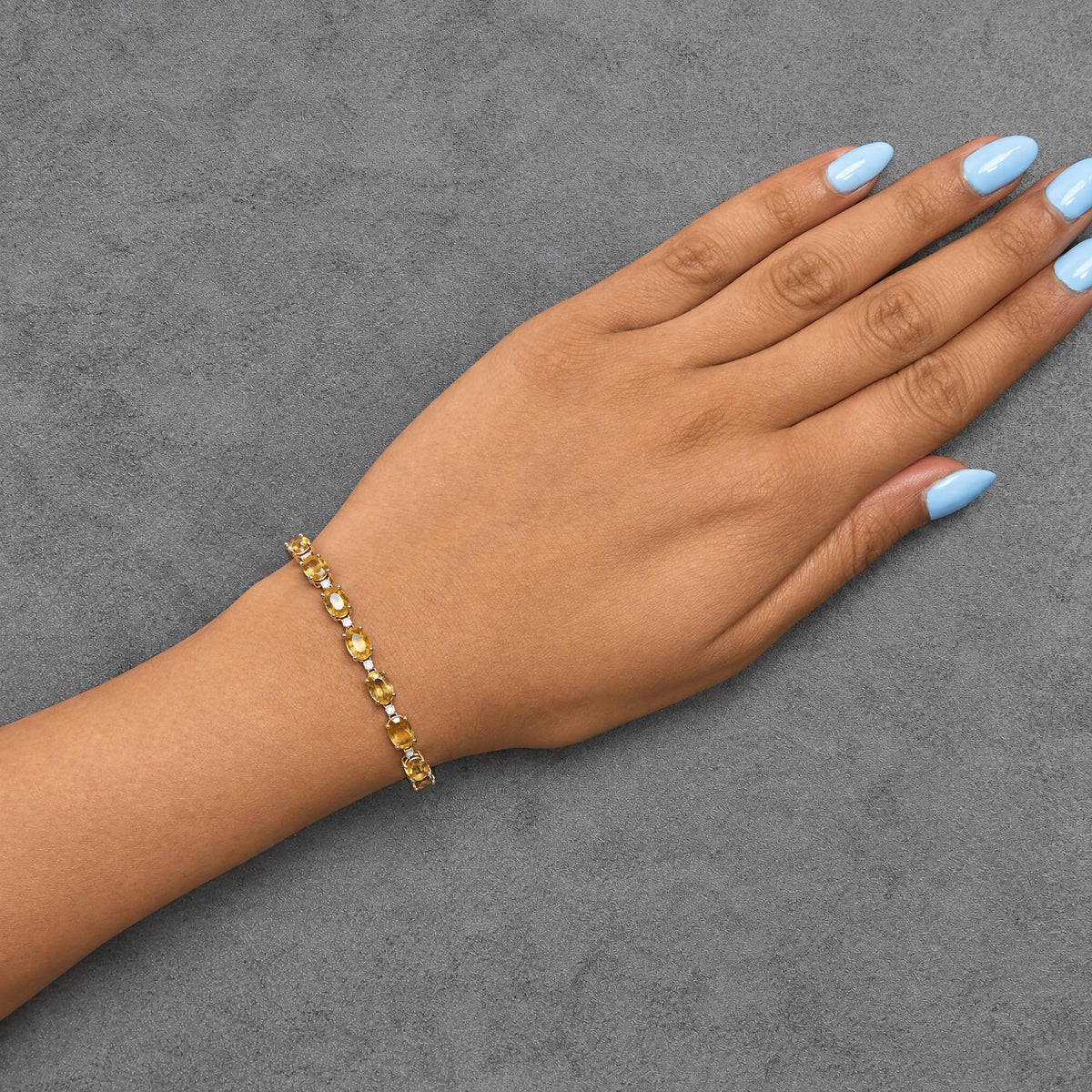 Close-up side angle of a model's hand wearing a white metal bracelet with alternating oval yellow gemstones and round white gemstones in prong settings.