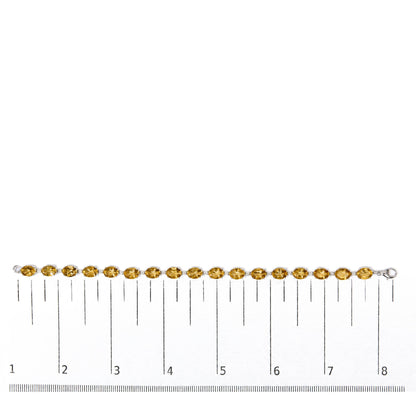 White metal bracelet with alternating yellow oval-shaped gemstones and small white round gemstones, shown flat on a scale from a top-down angle.