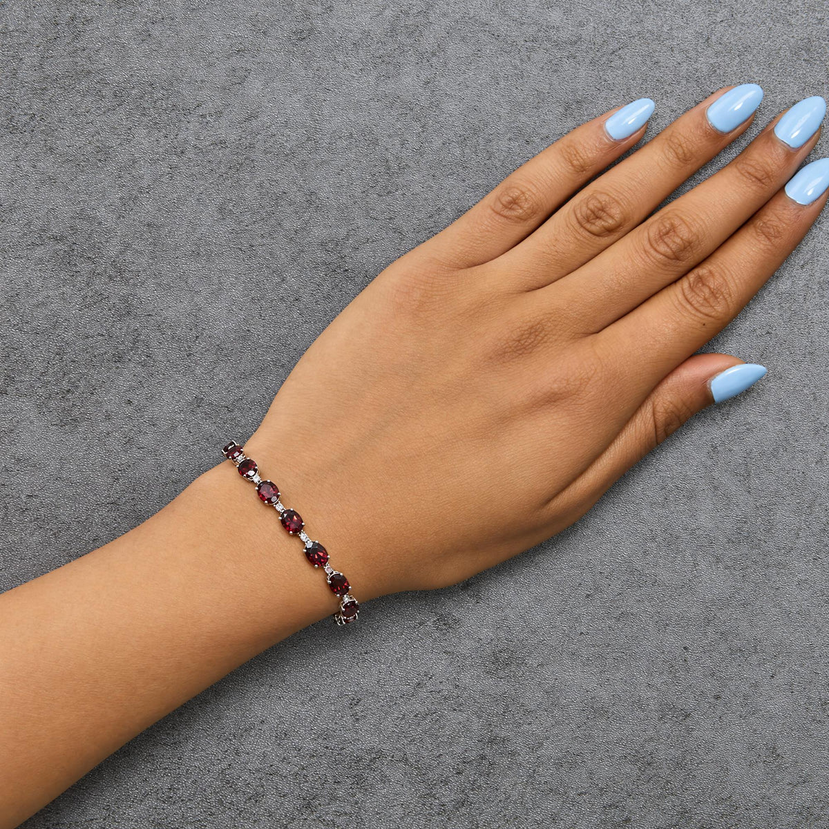 White metal bracelet with alternating round white gemstones and oval red gemstones in prong settings, shown worn on a model's wrist in a top-down angled shot.