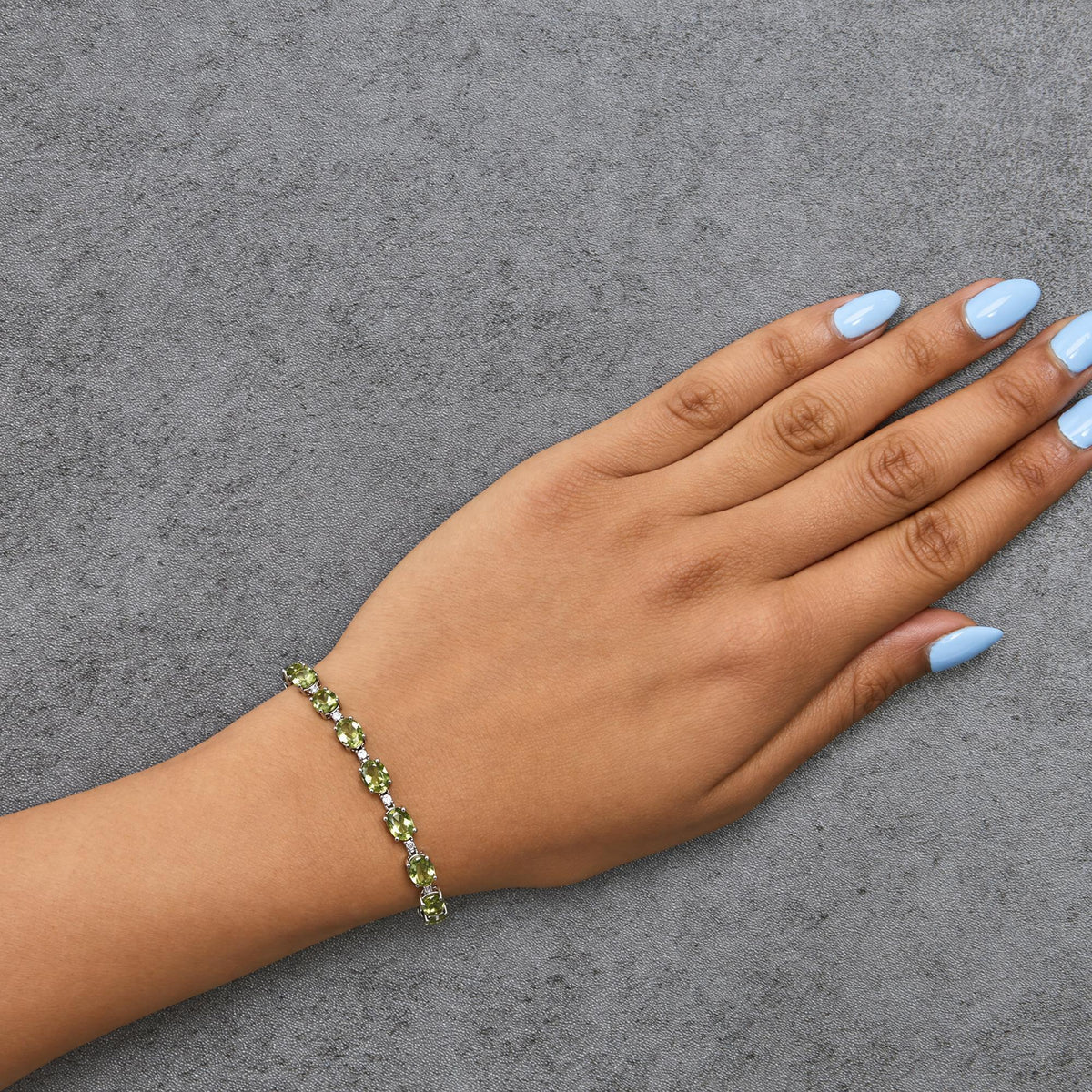 White metal bracelet with oval green gemstones and small white round gemstones in prong settings, shown worn on model's wrist, angled top view.