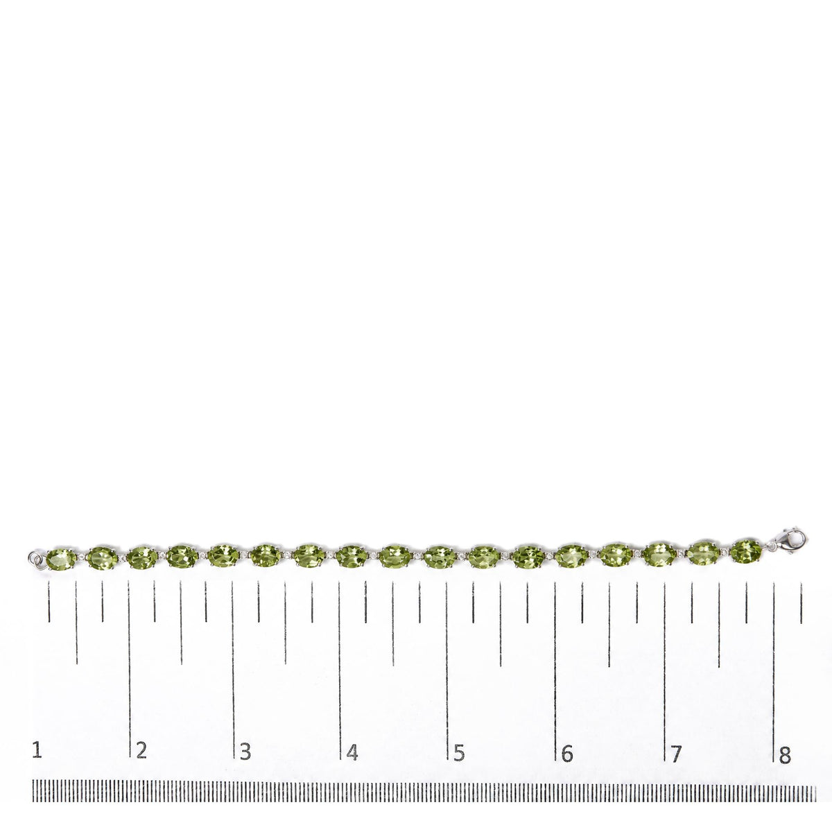 White metal bracelet with oval green gemstones and small round white gemstones set between them, shown on a measuring scale, top-down angle.