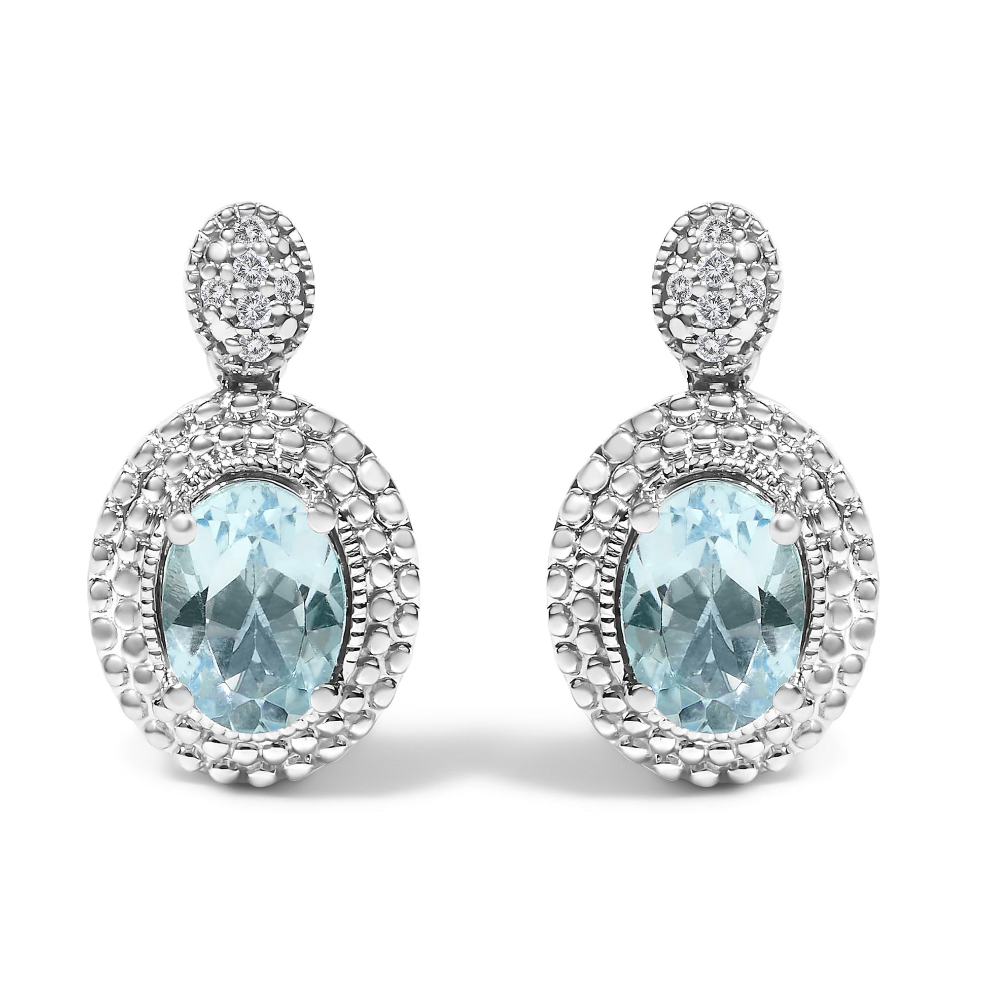 Front view of a pair of white metal earrings with oval blue gemstones set in the center, surrounded by pave-set round white gemstones, shown against a white background.