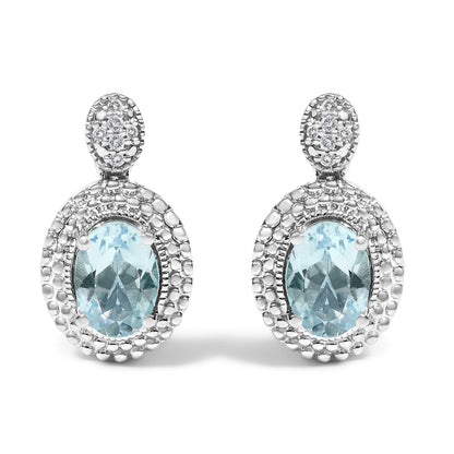 Front view of a pair of white metal earrings with oval blue gemstones set in the center, surrounded by pave-set round white gemstones, shown against a white background.