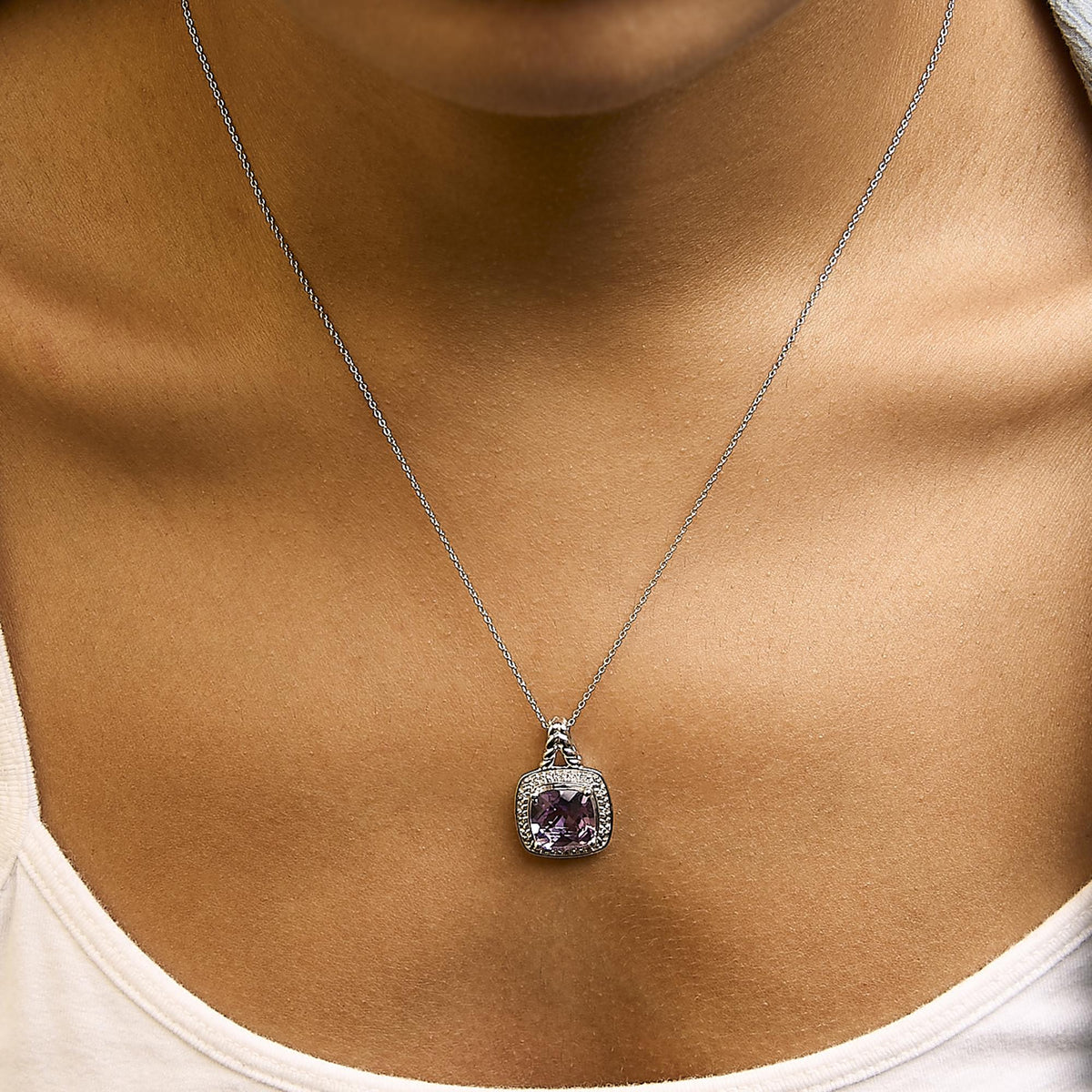 Close-up front view of a white metal necklace with a cushion-shaped purple gemstone pendant surrounded by small round white gemstones in a pave setting, shown worn on a model.