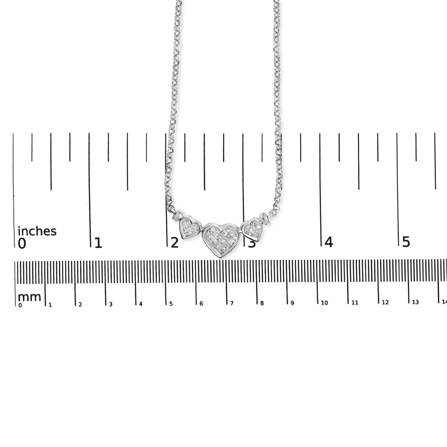 White metal necklace with three heart-shaped pendants set with white gemstones, shown hanging above a ruler for size reference, front view.