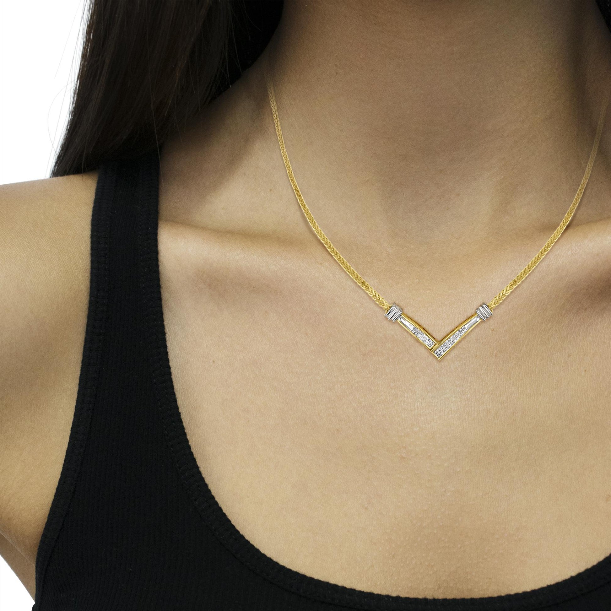 Close-up front view of a necklace on a model's neck featuring a yellow and white metal V-shaped pendant set with white gemstones in a channel setting.