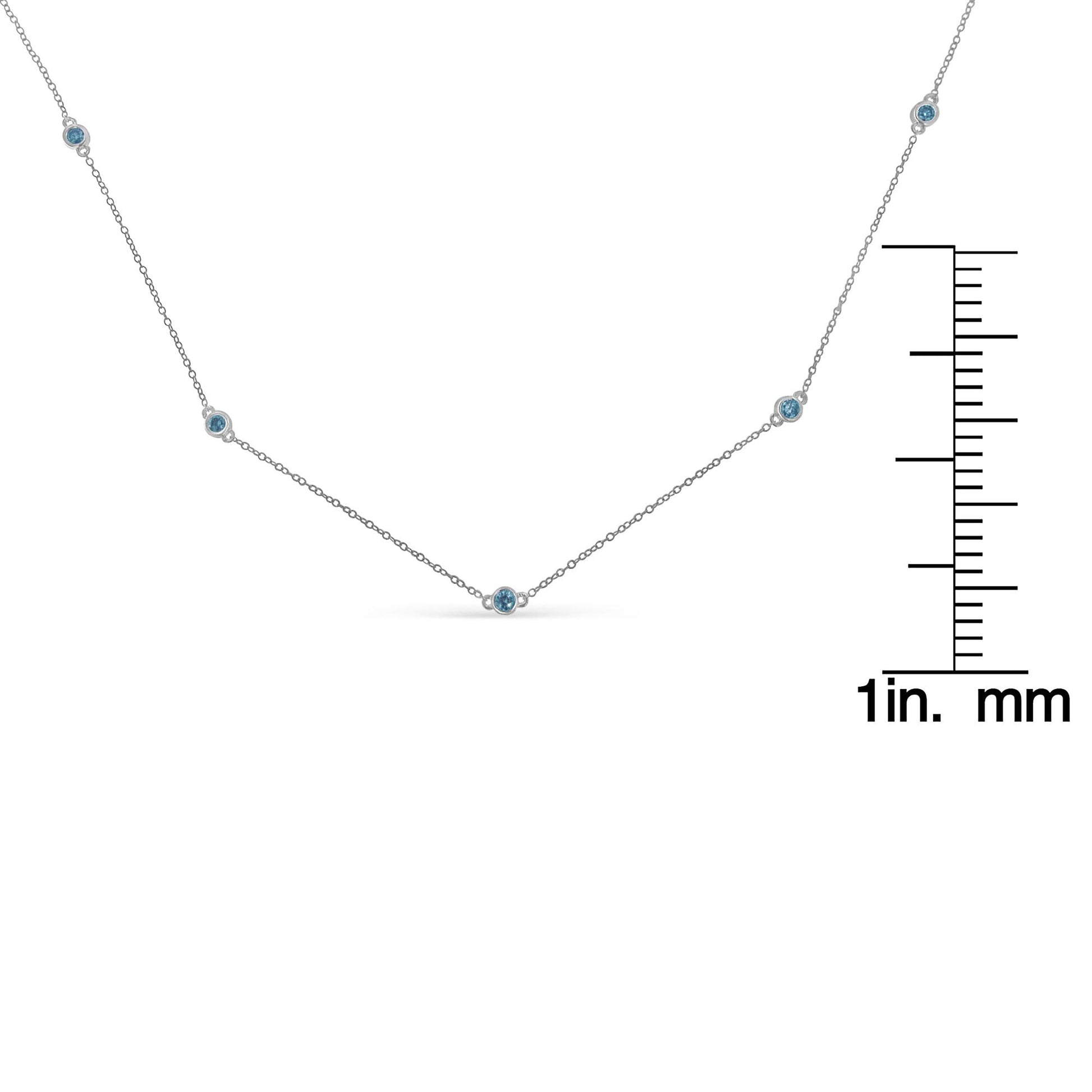 Front-facing shot of a white metal necklace with five round blue gemstones in bezel settings, displayed next to a ruler for size reference.