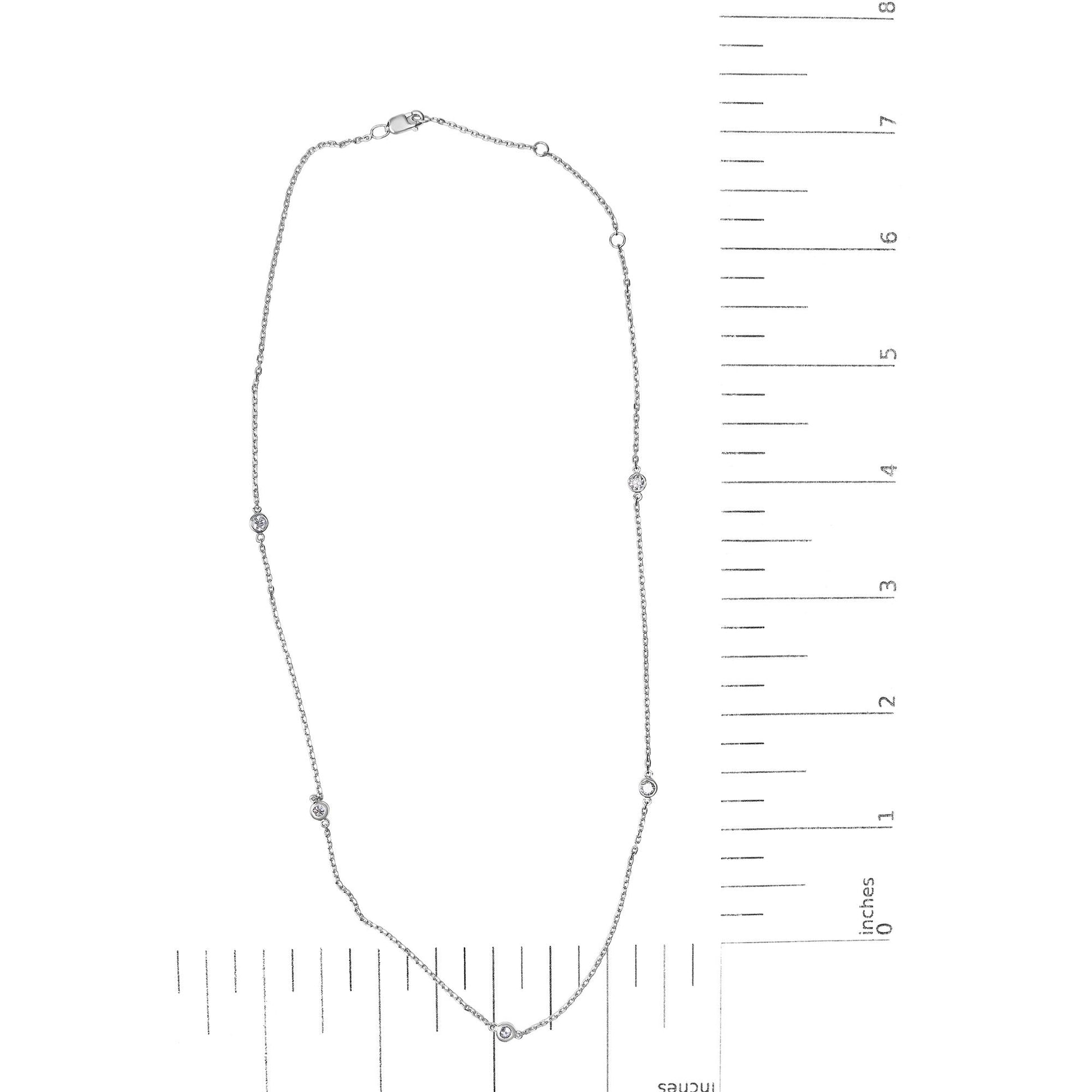 Top-down view of a white metal necklace with five round white gemstones in bezel settings, displayed on a ruler for size reference.