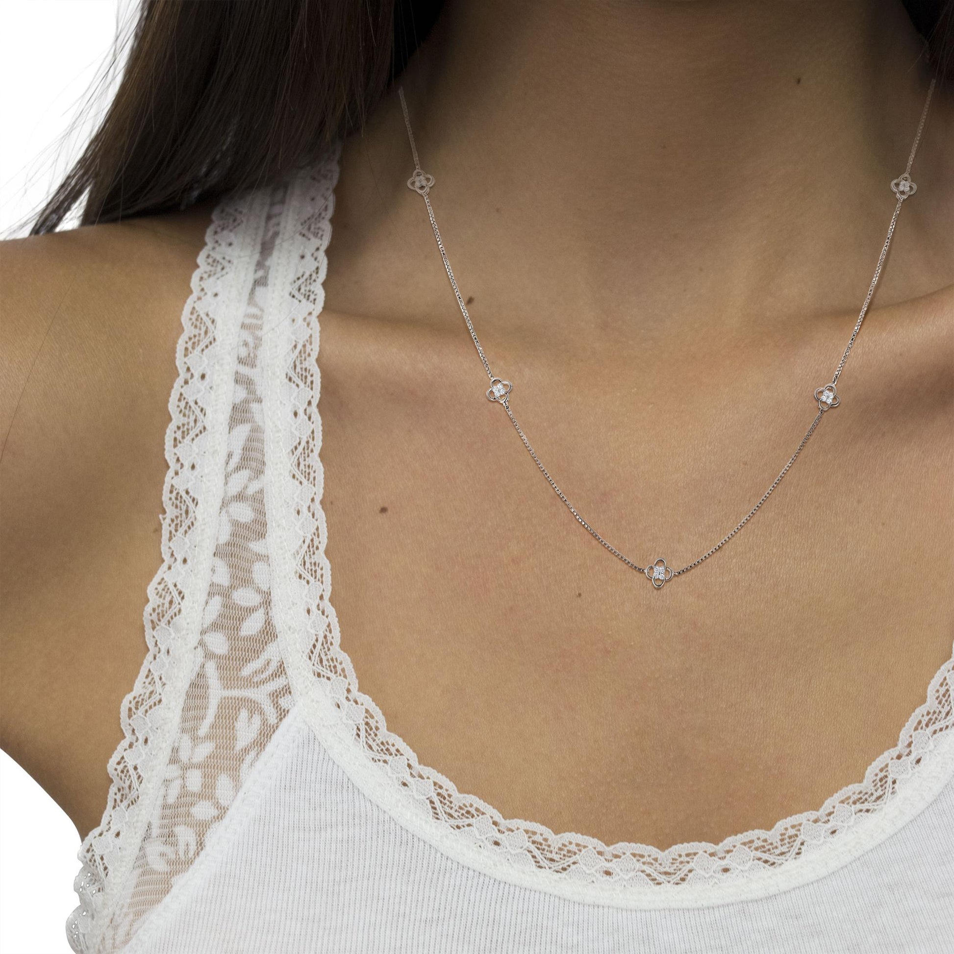 Close-up front angle of a white metal necklace with small four-petal floral motifs set with round white gemstones, worn on a model.