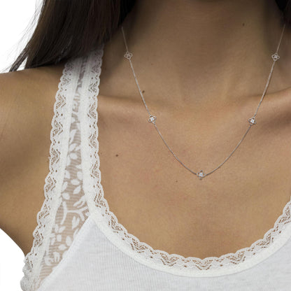 Close-up front angle of a white metal necklace with small four-petal floral motifs set with round white gemstones, worn on a model.