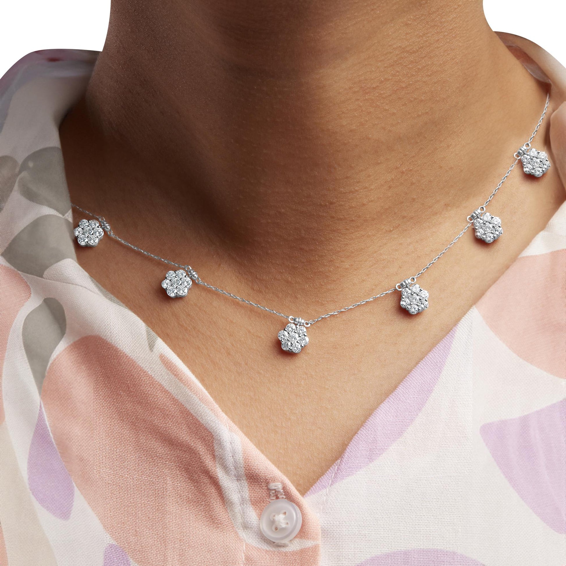 Close-up front view of a white metal necklace with multiple flower-shaped pendants each adorned with round white gemstones, worn on a model.