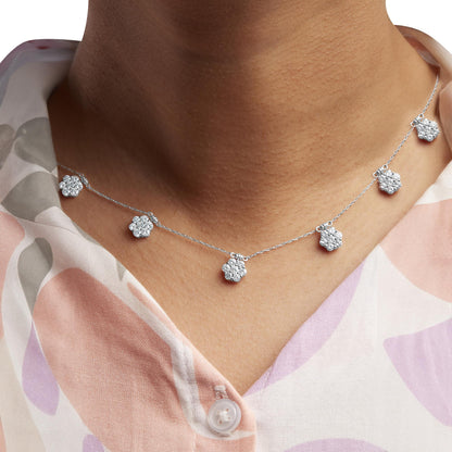 Close-up front view of a white metal necklace with multiple flower-shaped pendants each adorned with round white gemstones, worn on a model.