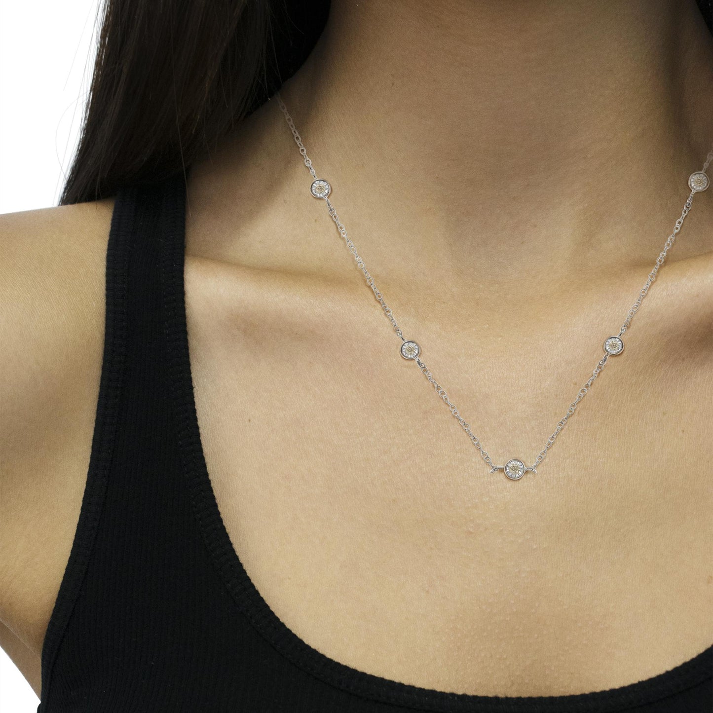 Close-up angled shot of a white metal necklace on a model, featuring round white gemstones set in a spaced pattern along the chain.