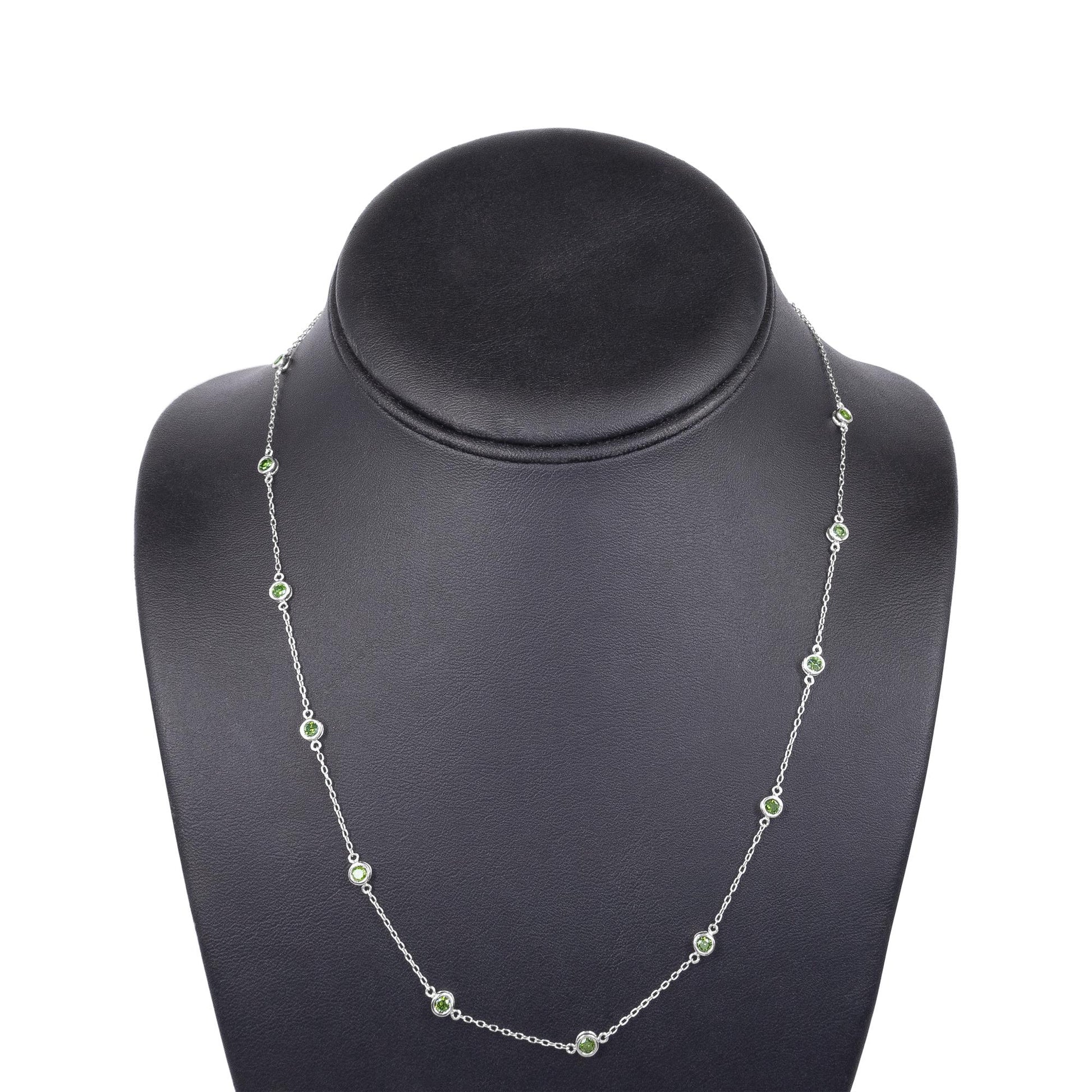 Front-facing shot of a white metal necklace with round green gemstones in bezel settings displayed on a black necklace stand.