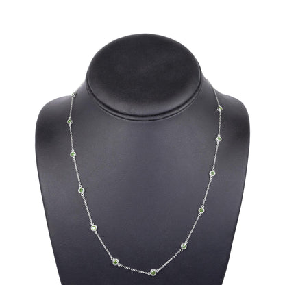 Front-facing shot of a white metal necklace with round green gemstones in bezel settings displayed on a black necklace stand.