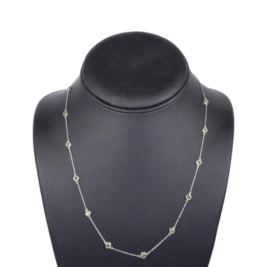 Front-facing shot of a white metal necklace with round green gemstones in bezel settings displayed on a black necklace stand.