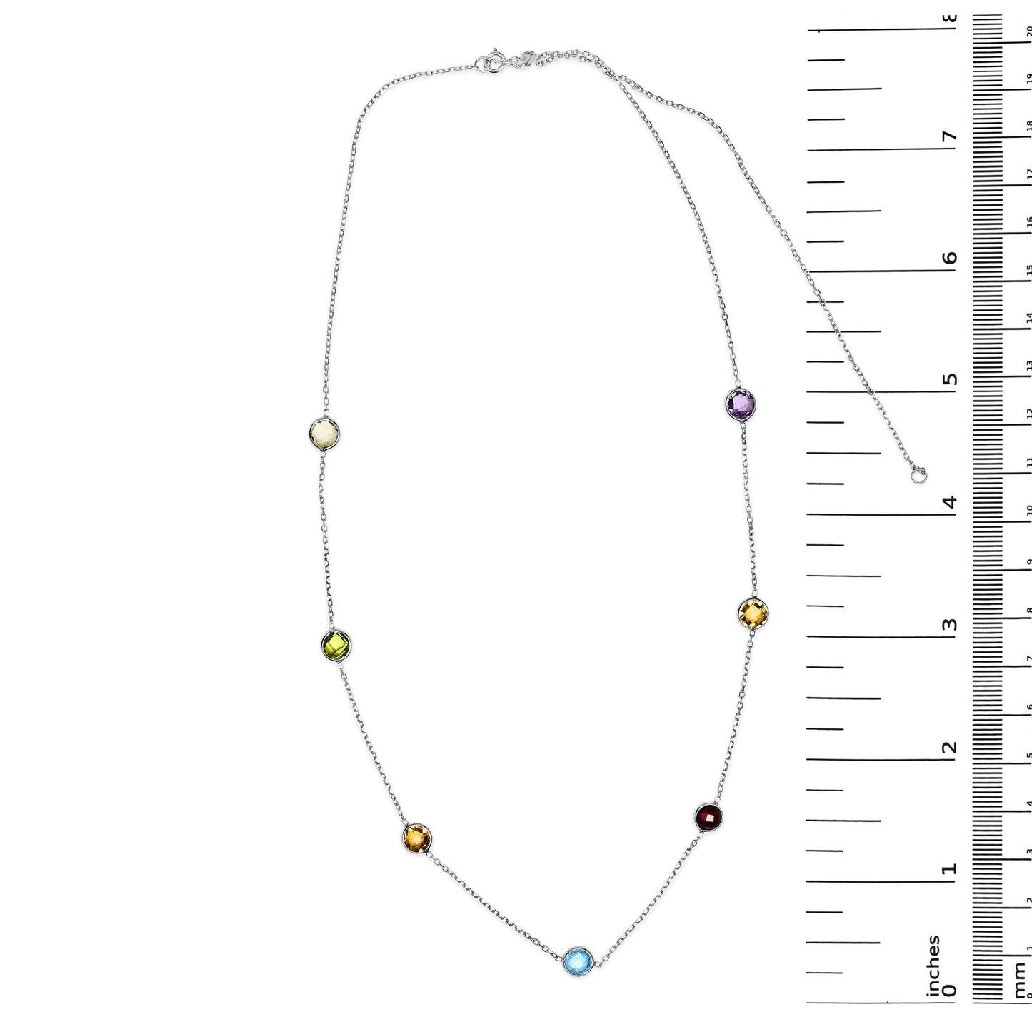 White metal necklace with round bezel-set gemstones in multiple colors including blue, purple, red, white, smoky, and yellow, displayed flat next to a ruler for size reference, top-down angle.