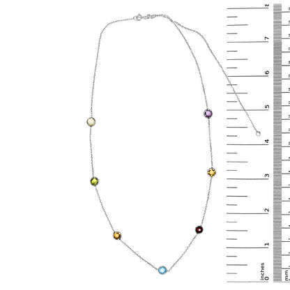 White metal necklace with round bezel-set gemstones in multiple colors including blue, purple, red, white, smoky, and yellow, displayed flat next to a ruler for size reference, top-down angle.