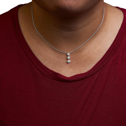 Close-up front view of a white metal necklace on a model wearing a red top, featuring a vertical pendant with three princess-shaped white gemstones in bezel settings.