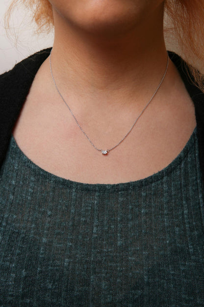 Close-up front view of a model wearing a white metal necklace with a small oval white gemstone in a four-prong setting at the center.