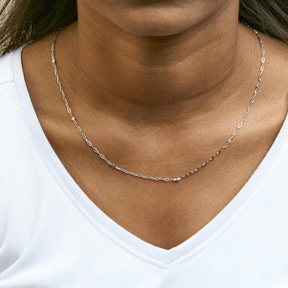 Close-up front view of a white metal necklace with a delicate chain featuring small round white gemstones in bezel settings, shown worn on a model.