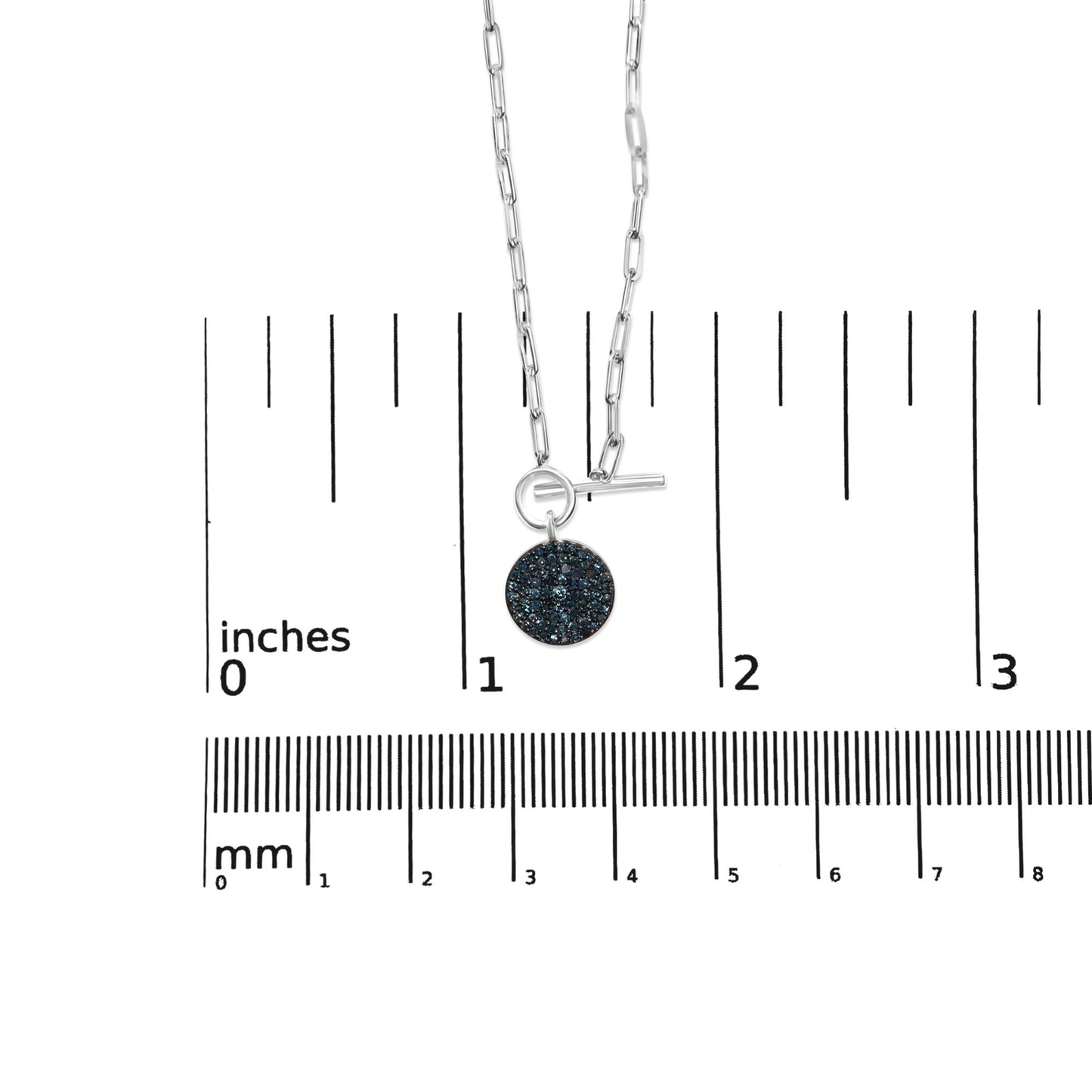 Close-up front view of a white metal necklace with a round pendant covered in multiple small blue gemstones, placed on a ruler for size reference.