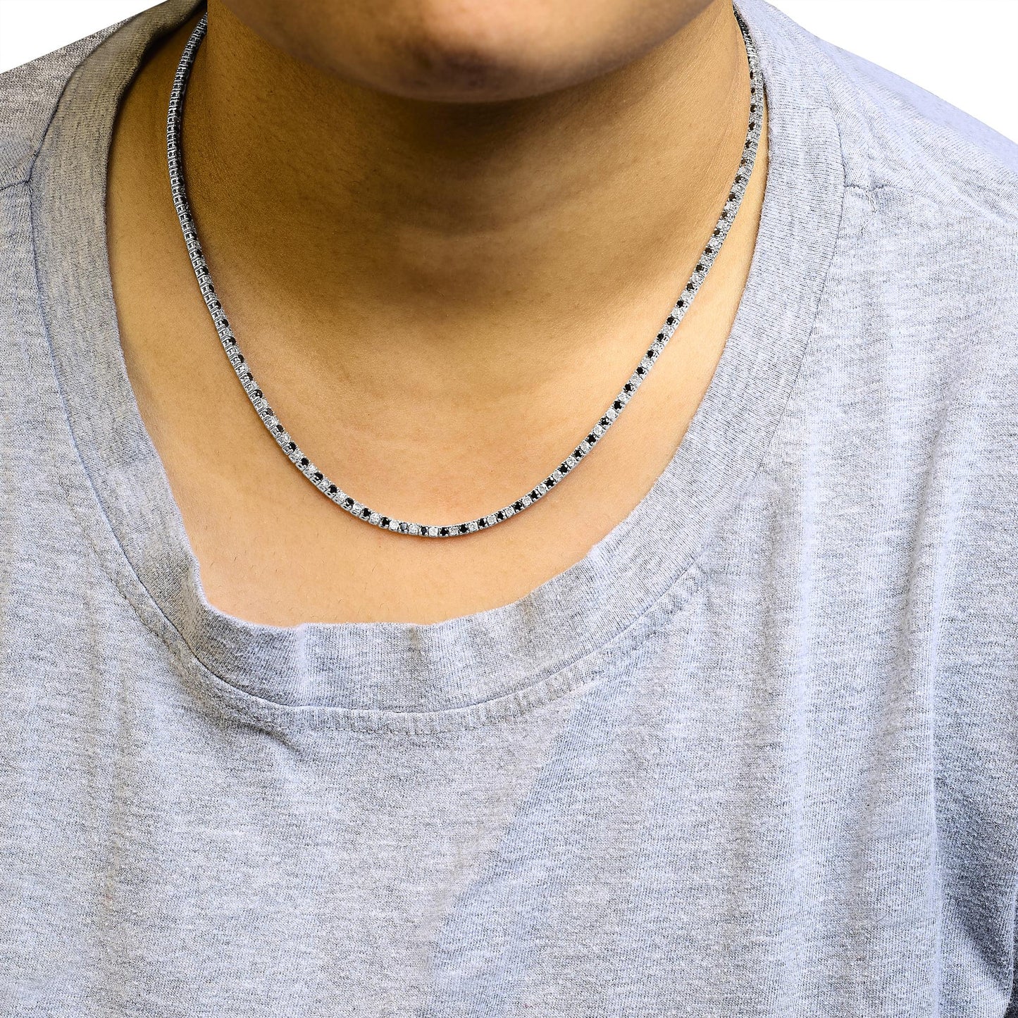 Close-up front view of a white metal necklace with alternating white and black round gemstones in four-prong settings, worn on a model wearing a light gray shirt.