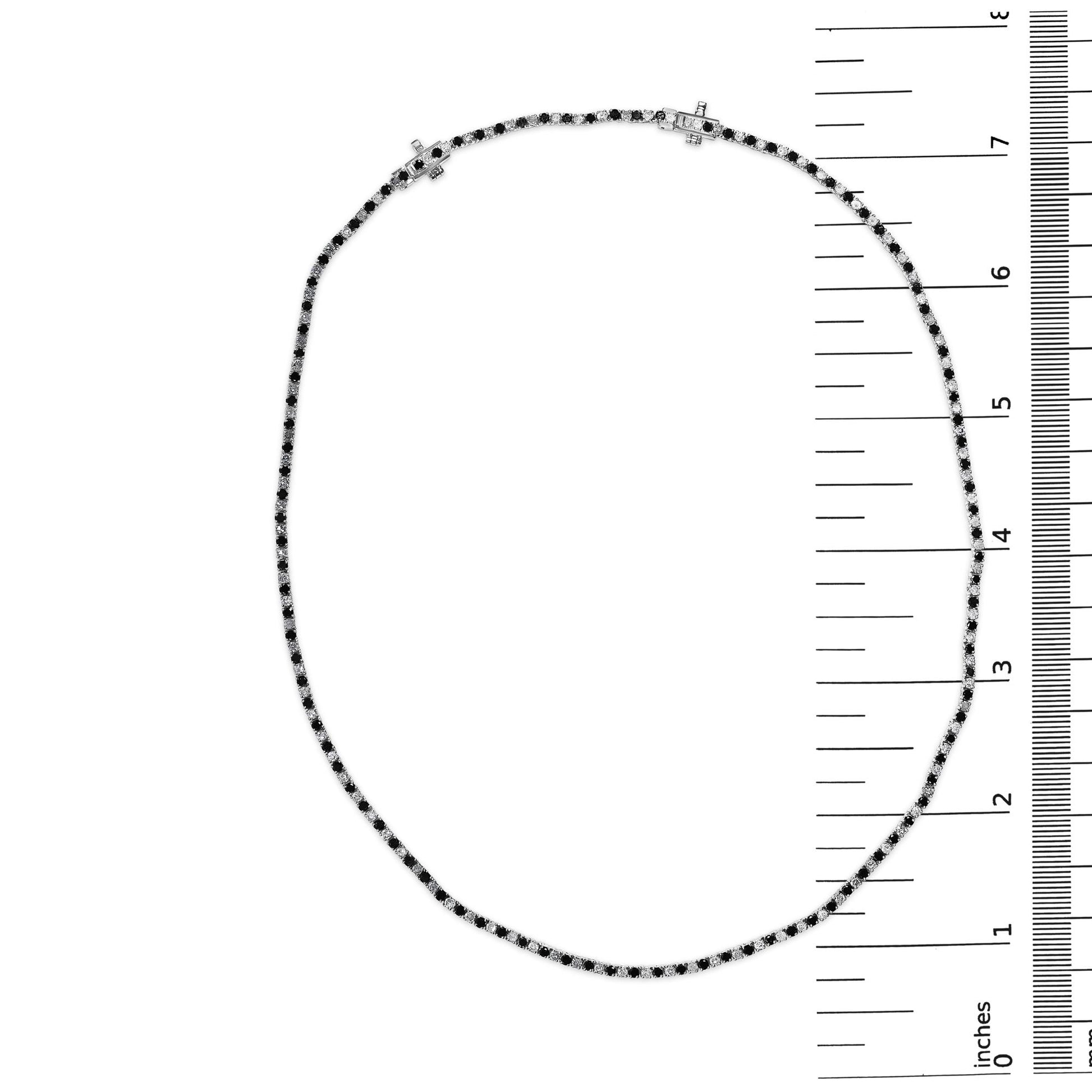Top-down view of a white metal necklace with alternating black and white round gemstones in prong settings, displayed on a ruler for size reference.