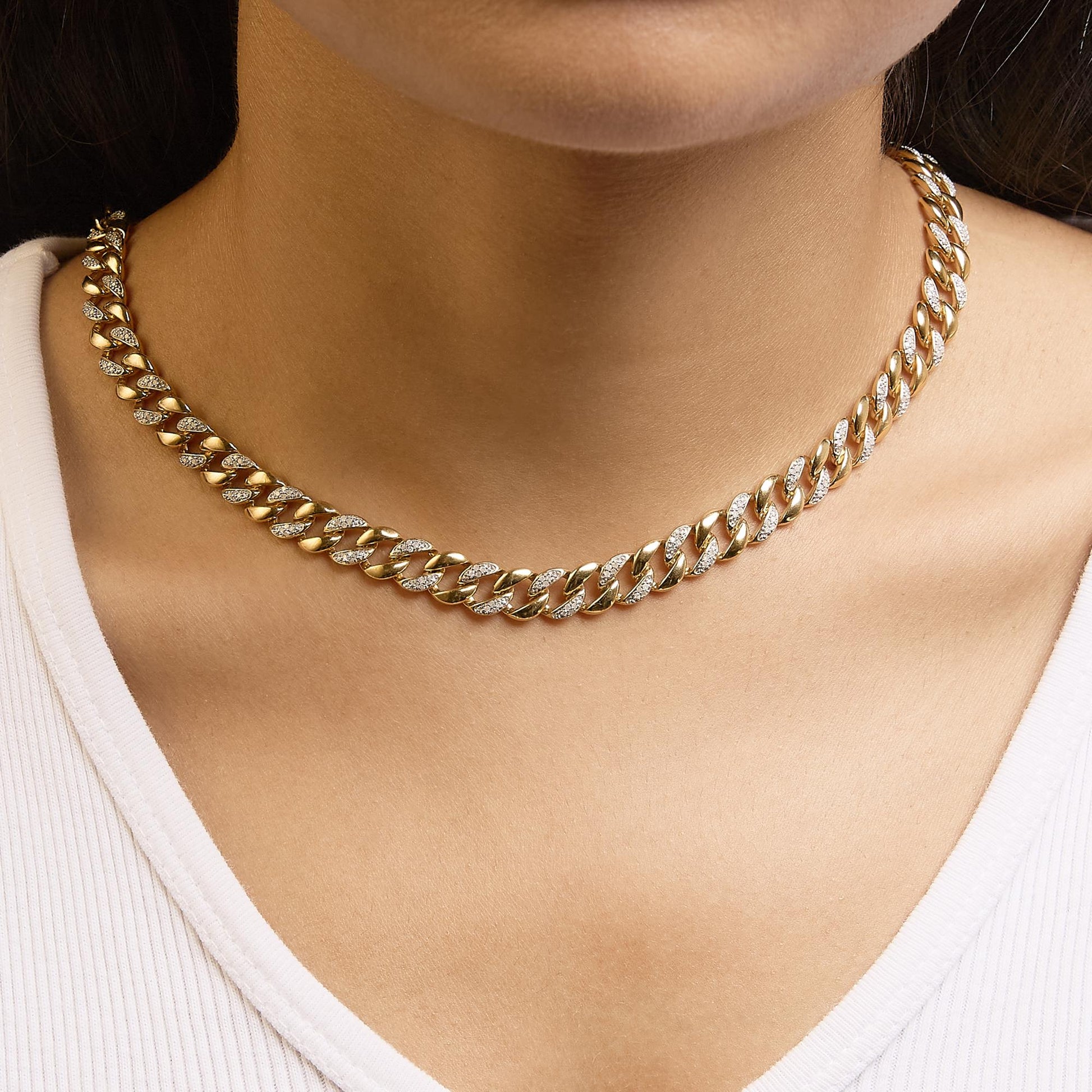 Close-up front view of a yellow metal necklace with alternating plain and white gemstone-studded links, worn on a model's neck.