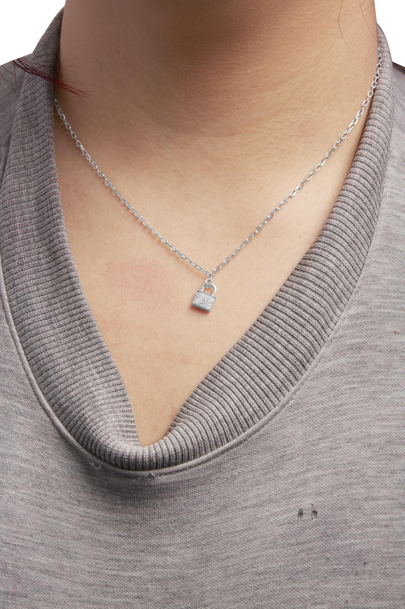 Close-up front view of a white metal necklace with a small padlock-shaped pendant adorned with round white gemstones in prong settings, worn on a model.
