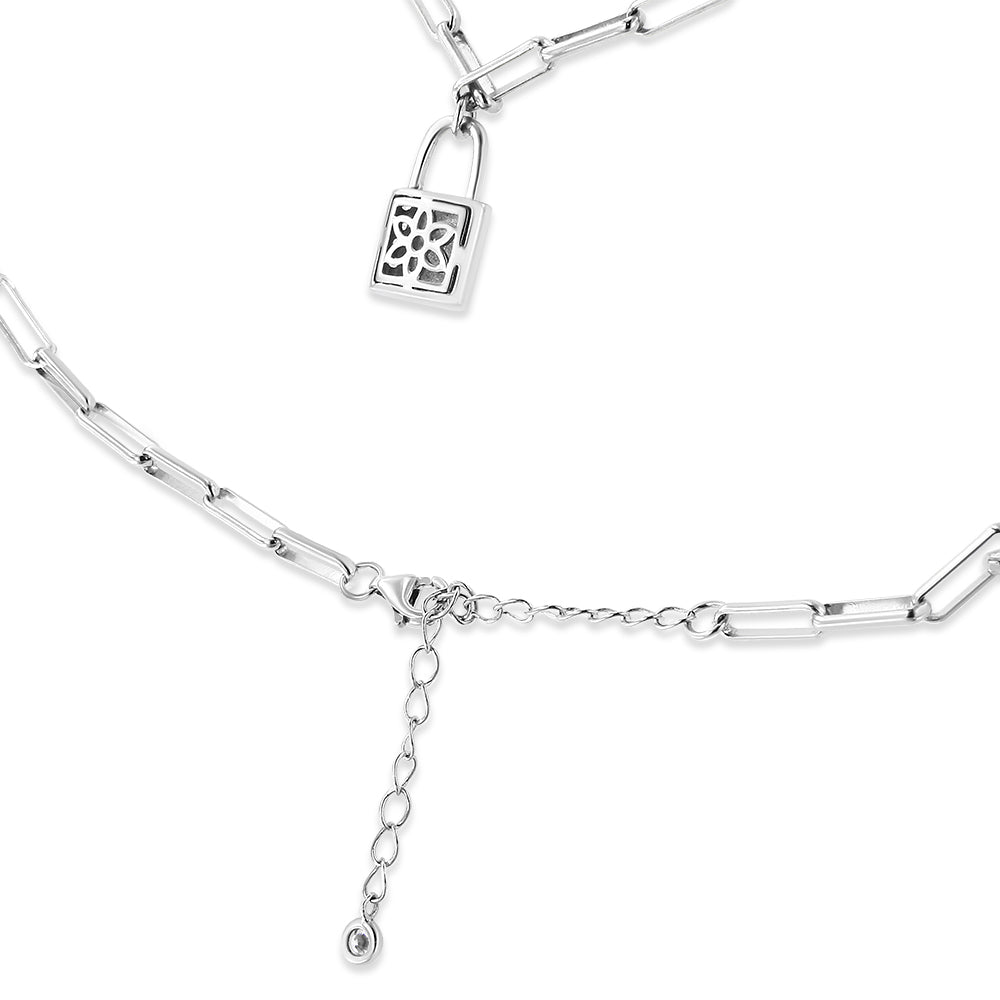 Close-up image of a white metal necklace with elongated chain links, featuring a small padlock charm with a floral cutout design and a dangling chain with a white gemstone at the end, shown from a slightly angled top view.