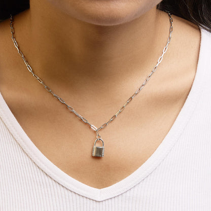 White metal necklace with a padlock pendant accented by white round gemstones in prong settings, shown from a front angle on a model wearing a white top.