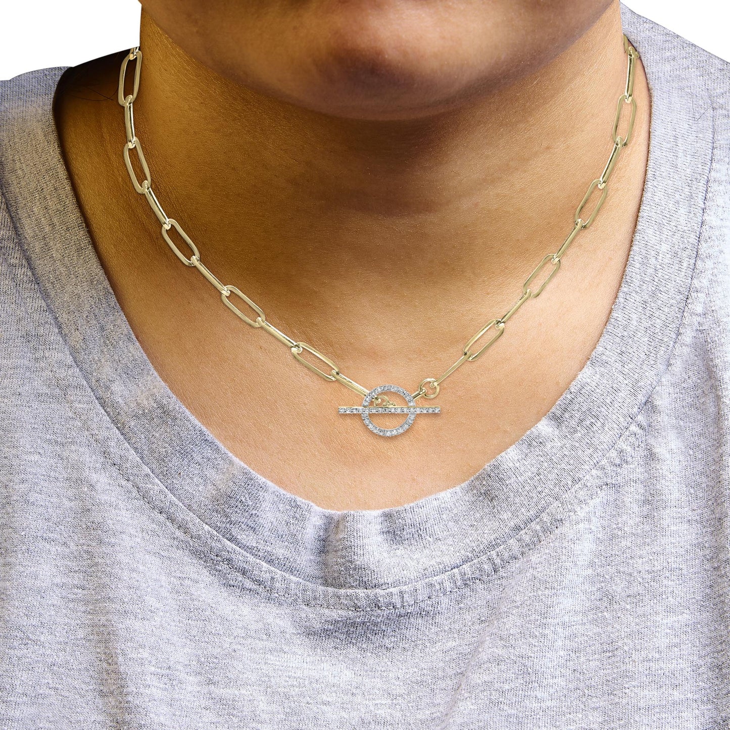 Close-up front view of a yellow metal link necklace with a toggle clasp set with white round gemstones, worn on a model.