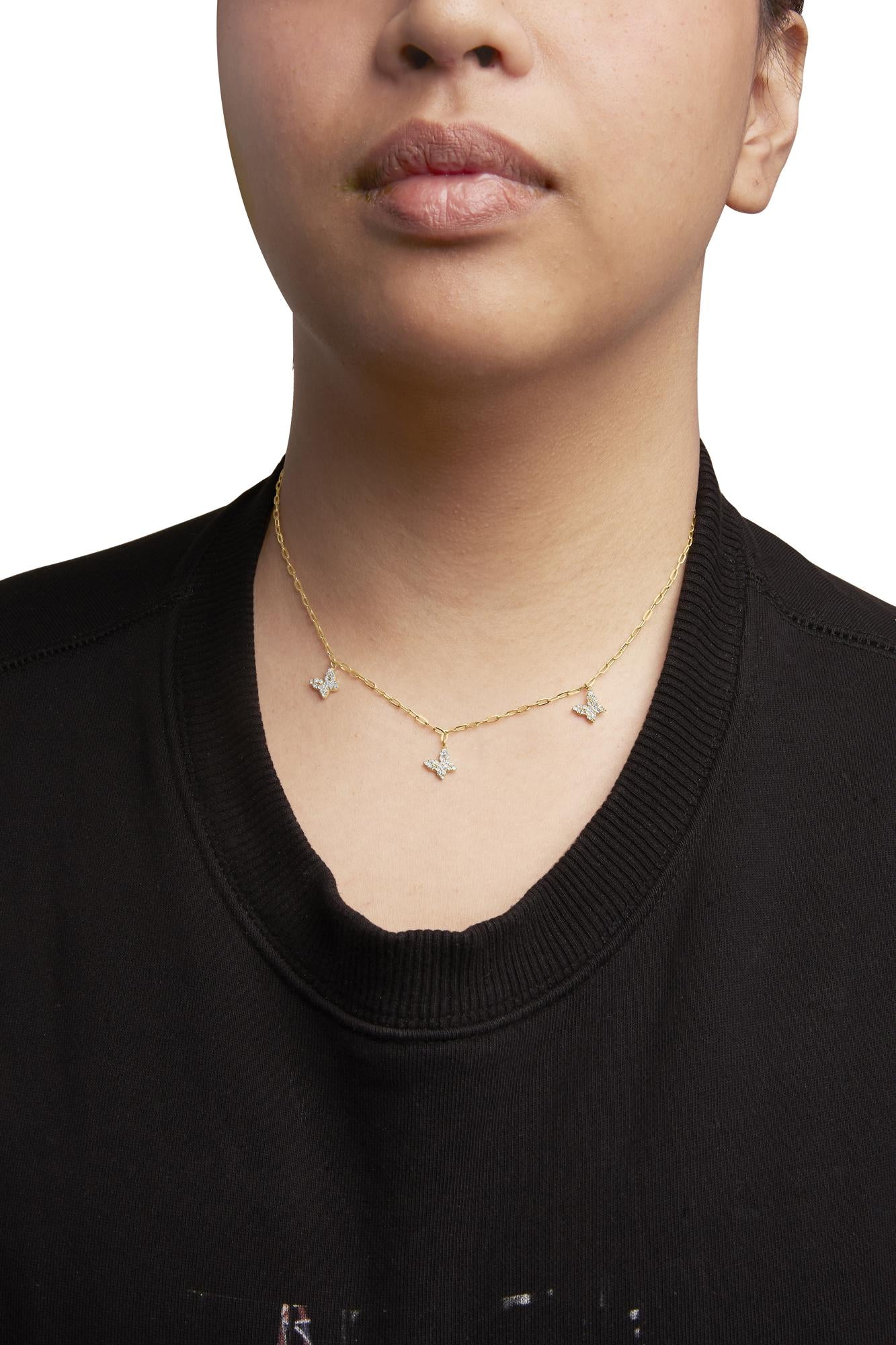 Yellow metal necklace with three butterfly-shaped clusters of white round prong-set gemstones, worn on a model, front-facing close-up view.