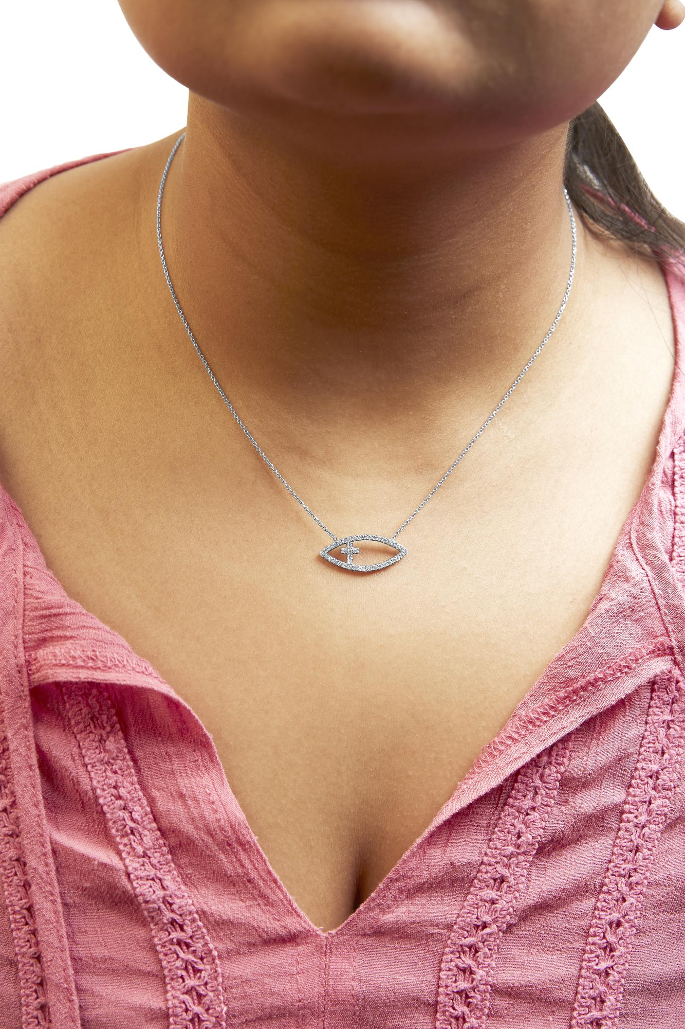 Close-up front view of a white metal necklace with a fish-shaped pendant adorned with round white gemstones in prong setting, worn on a model with a pink textured top.