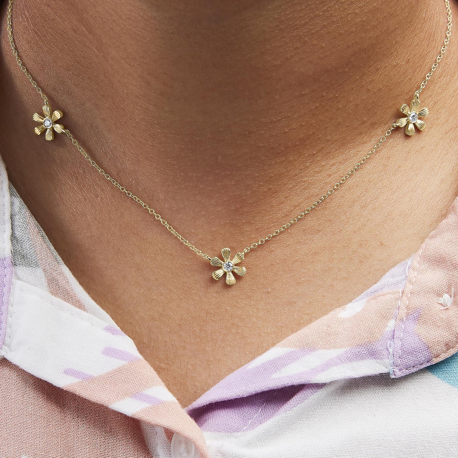 Close-up front view of a yellow metal necklace on a model with three small flower-shaped pendants, each featuring a round white gemstone in the center.