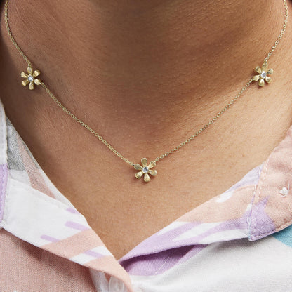 Close-up front view of a yellow metal necklace on a model with three small flower-shaped pendants, each featuring a round white gemstone in the center.